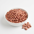 Dry shelled groundnuts with reddish skins in a white bowl on a white background