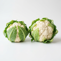 Two fresh white cauliflower heads with green leaves on white background